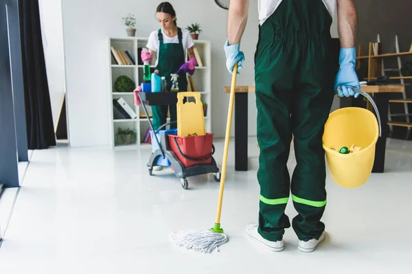 Recortado de jóvenes trabajadores de la empresa de limpieza que tienen varios equipos de limpieza en la oficina - foto de stock