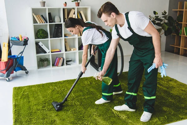 Young cleaning company workers cleaning carpet with vacuum cleaner and detergent spray — Stock Photo