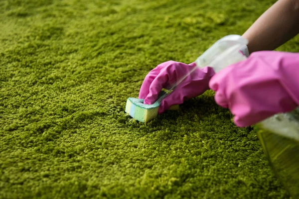 Gros plan vue partielle de la personne dans des gants en caoutchouc nettoyage tapis avec chiffon et pulvérisation de détergent — Photo de stock