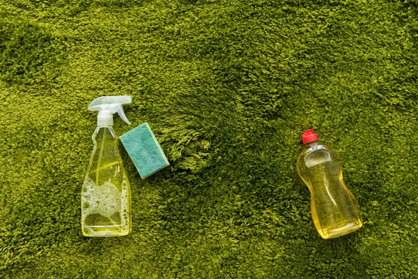 Vue rapprochée des bouteilles avec détergent et chiffon sur tapis vert avec espace de copie — Photo de stock