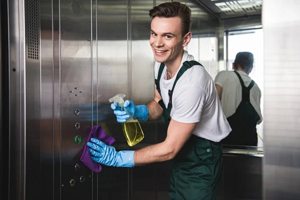 Jovem empresa de limpeza trabalhador limpeza elevador e sorrindo para a câmera — Fotografia de Stock