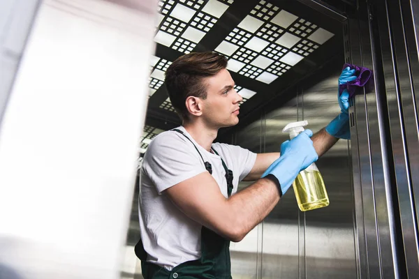 Low angle view of handsome young cleaner washing elevator with rag and detergent — Stock Photo