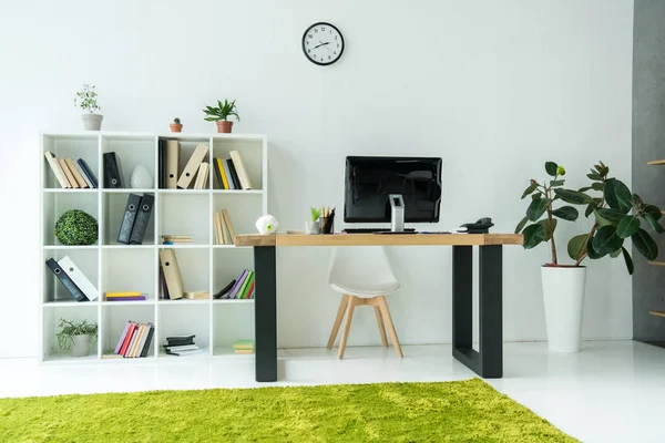 Interior de escritório moderno com monitor de computador na mesa e livros com pastas em prateleiras — Fotografia de Stock