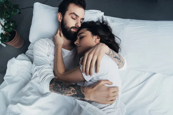 Bela jovem tatuado casal abraçando enquanto dorme na cama — Fotografia de Stock