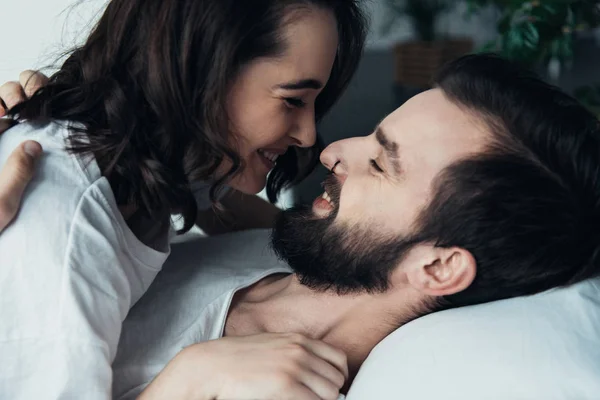 Felice giovane coppia sorridente, guardarsi l'un l'altro e abbracciarsi mentre si trova a letto a casa — Foto stock