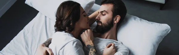 Junges Paar schaut einander an und umarmt sich, während sie zu Hause im Bett liegen — Stockfoto