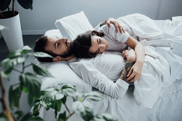 Beautiful young couple in pajamas embracing while lying in bed at home — Stock Photo