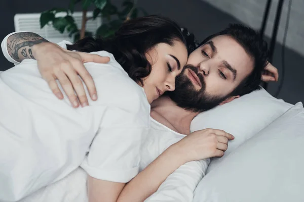 Belo jovem casal abraçando enquanto deitado na cama em casa — Fotografia de Stock