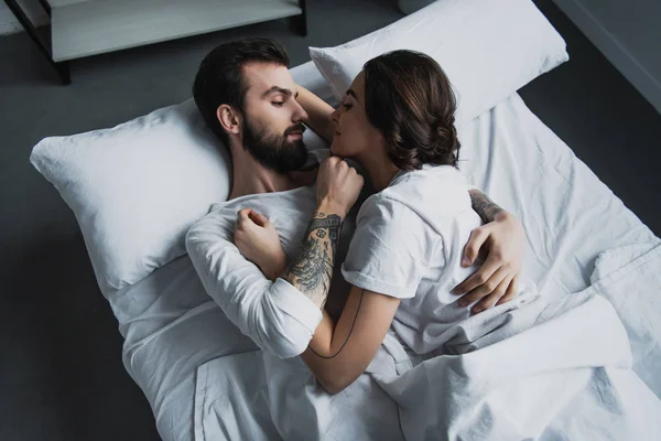 Attractive young couple in pajamas embracing while lying in bed at home — Stock Photo