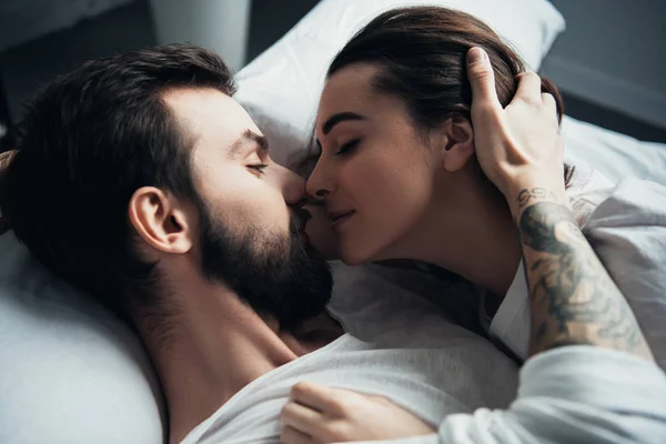 Guapo tatuado hombre abrazando hermosa mujer mientras está acostado en la cama - foto de stock