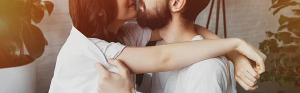 Vista recortada de pareja joven abrazándose en casa con la luz del sol en el fondo - foto de stock