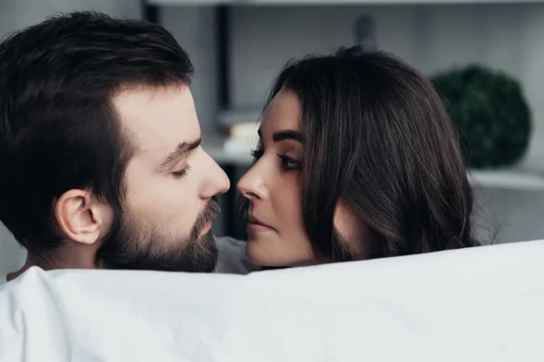 Hermosa romántica joven pareja sosteniendo manta y mirando el uno al otro en casa - foto de stock