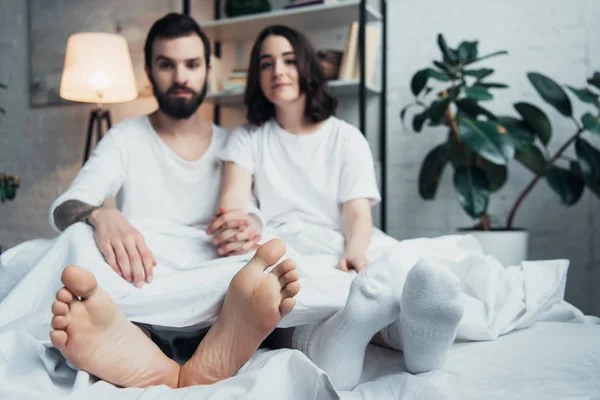 Jeune couple en pyjama couché dans le lit et regardant la caméra à la maison — Photo de stock