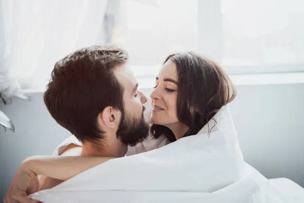 Schönes junges glückliches Paar, in eine Decke gehüllt, umarmt und sieht sich zu Hause an — Stockfoto