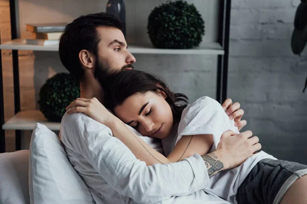 Atraente jovem tatuado casal abraçando enquanto deitado na cama em casa — Fotografia de Stock