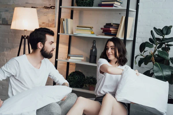 Hermosa joven pareja en pijama teniendo almohada lucha en casa - foto de stock