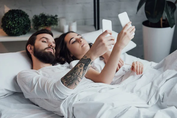 Schönes junges Paar liegt im Bett und benutzt Smartphones — Stockfoto