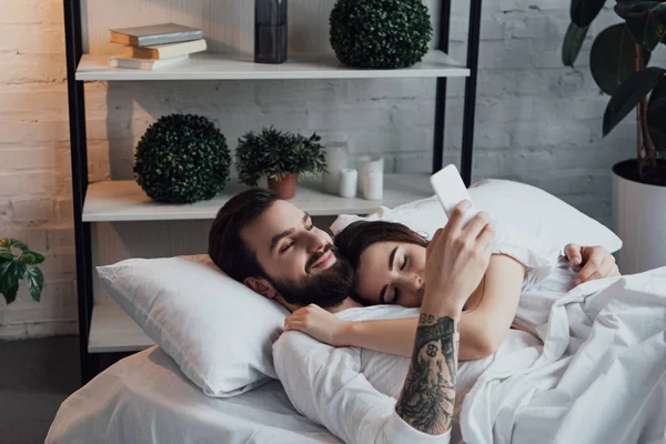 Bell'uomo che utilizza lo smartphone mentre la donna dorme a letto — Foto stock