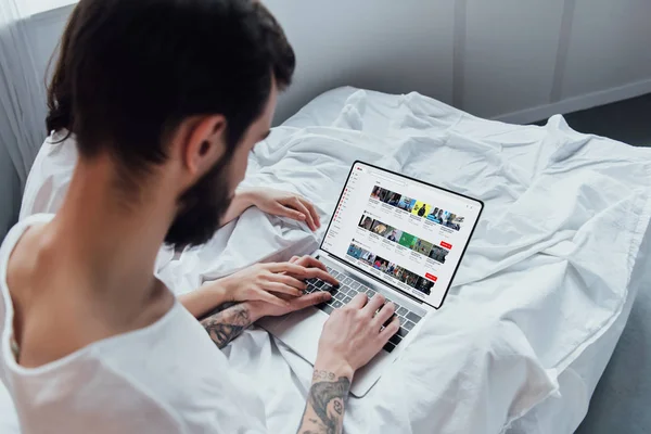Rückansicht des Paares, das im Bett liegt, Hände hält und Laptop mit youtube-Webseite auf dem Bildschirm benutzt — Stockfoto