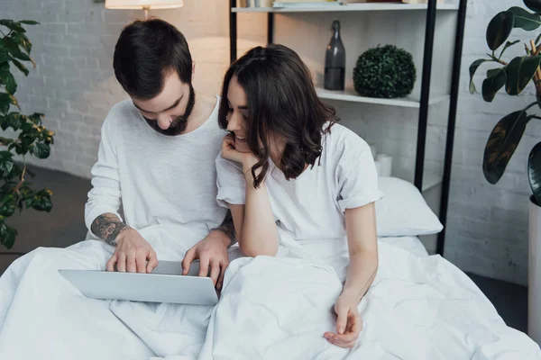 Hermosa pareja joven en pijama acostado en la cama y el uso de la computadora portátil - foto de stock