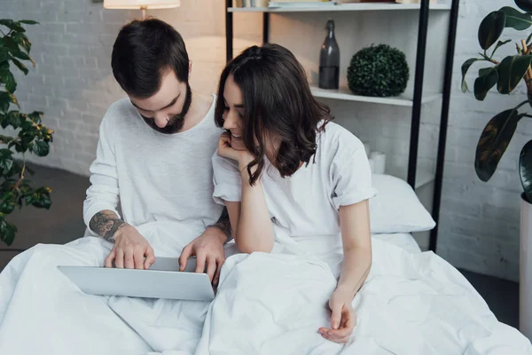 Belo jovem casal de pijama deitado na cama e usando laptop — Fotografia de Stock