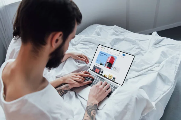 Vue arrière du couple couché au lit, tenant la main et utilisant un ordinateur portable avec le site Web ebay à l'écran — Photo de stock