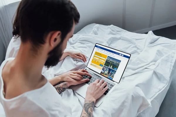 Back view of couple lying in bed, holding hands and using laptop with booking website on screen — Stock Photo