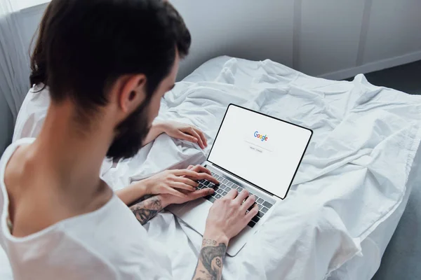 Vue arrière du couple couché au lit, tenant la main et utilisant un ordinateur portable avec google site Web à l'écran — Photo de stock