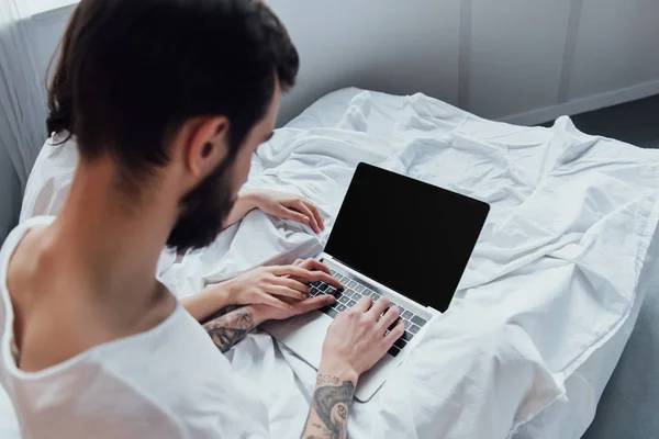 Back view of couple holding hands and using laptop with blank screen at home in bed — Stock Photo