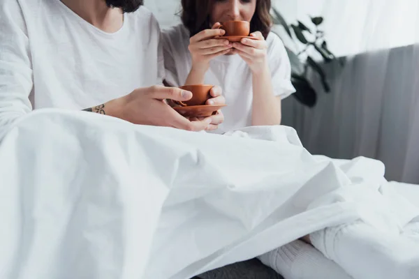 Частичный вид молодой пары, лежащей в постели и пьющей кофе утром — стоковое фото