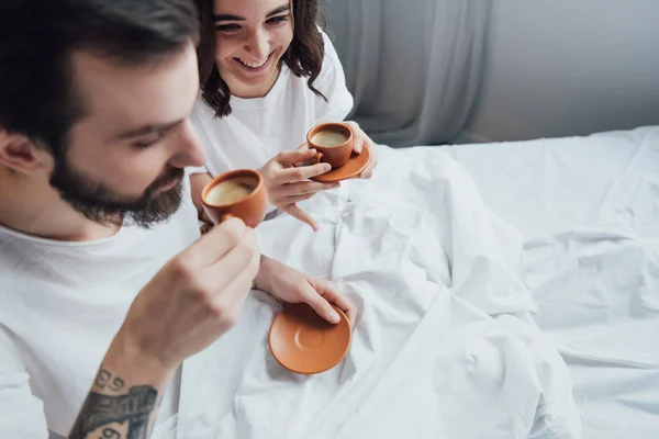 Красива молода пара п'є каву, лежачи в ліжку вранці — стокове фото