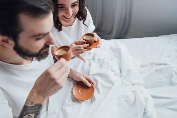 Beautiful young couple drinking coffee while lying in bed in morning — Stock Photo