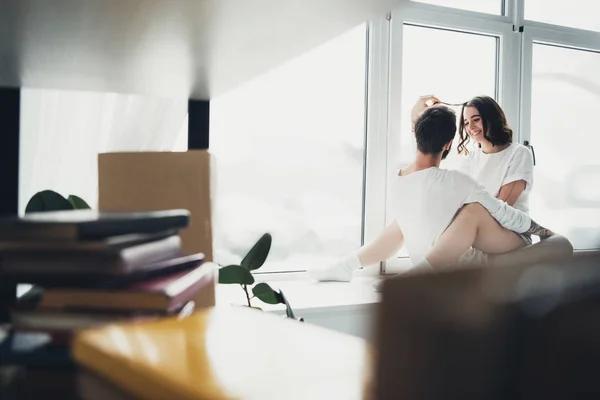 Selective focus of beautiful young couple hugging and sitting on window sill at home with copy space — Stock Photo