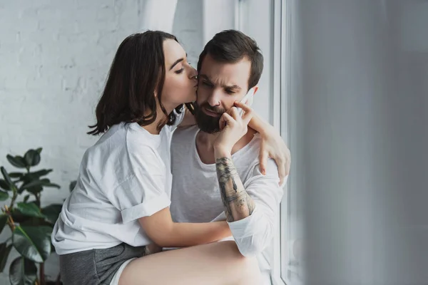 Bella donna baciare uomo parlando su smartphone a casa — Foto stock