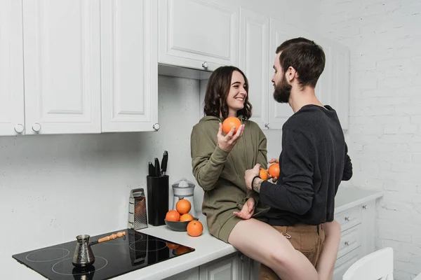Schönes junges glückliches Paar hält Orangen in der Hand und schaut einander in der Küche an — Stockfoto