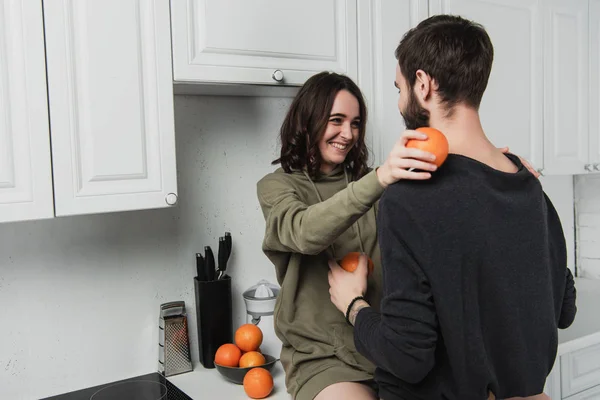 Beautiful young happy couple holiding oranges and looking at each other in kitchen — Stock Photo