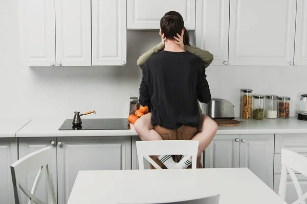 Vista posteriore della giovane coppia che abbraccia e bacia a kithchen durante la colazione — Foto stock