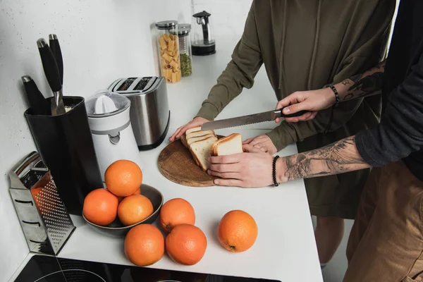 Vue recadrée du couple préparant le petit déjeuner et coupant le pain en cuisine — Photo de stock