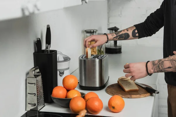 Обрізаний вид татуйованого чоловіка готує тости з тостером під час сніданку на кухні — стокове фото