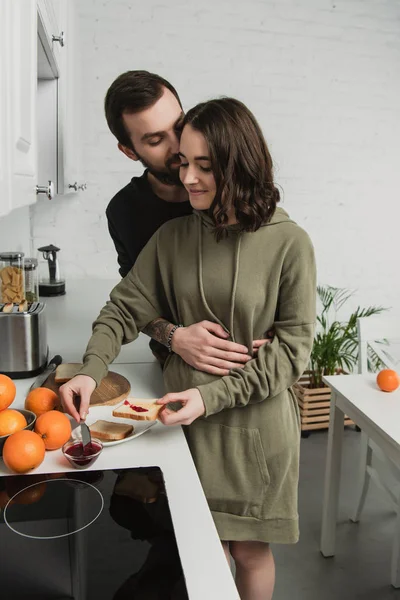 Hermosa pareja joven preparando brindis durante el desayuno en la cocina - foto de stock