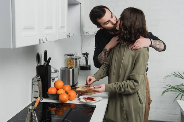 Belo jovem casal beijando enquanto prepara torradas durante o café da manhã na cozinha — Fotografia de Stock