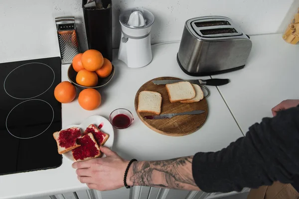 Vista cortada do homem preparando torradas com geléia durante o café da manhã na cozinha — Fotografia de Stock