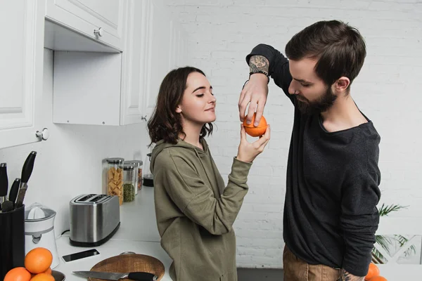 Hermosa pareja joven sosteniendo naranja en la cocina durante el desayuno - foto de stock