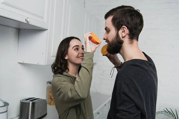 Beautiful smiling young couple holding oranges in kitchen — Stock Photo