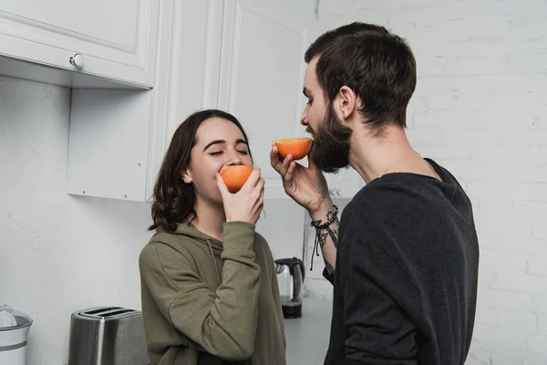 Hermosa pareja joven comer naranjas en la cocina - foto de stock