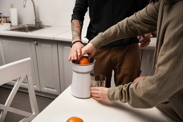 Vista parcial de la pareja preparando jugo de naranja durante el desayuno en la cocina - foto de stock