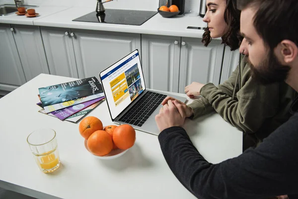 Пара сидит за столом и с помощью ноутбука с бронированием веб-сайт на экране на кухне — стоковое фото