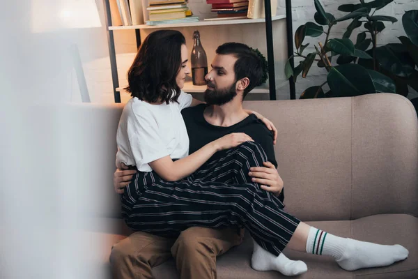 Bella giovane coppia guardando l'un l'altro e abbracciando mentre seduto sul divano in soggiorno — Foto stock