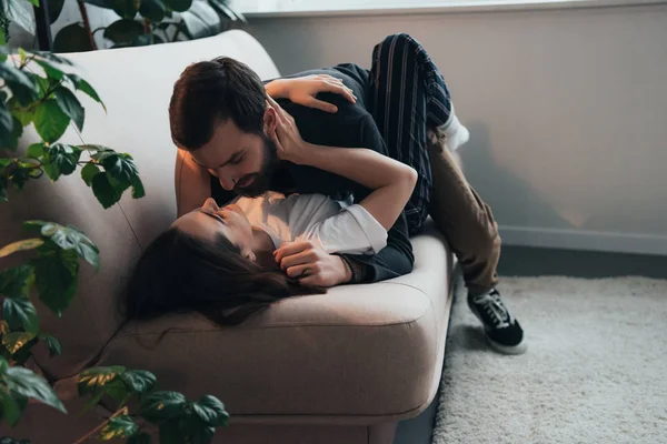 Jeune couple passionné embrasser tout allongé sur le canapé à la maison — Photo de stock