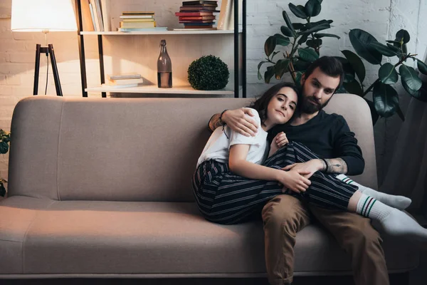 Belo jovem casal abraçando enquanto sentado no sofá na sala de estar com espaço de cópia — Fotografia de Stock